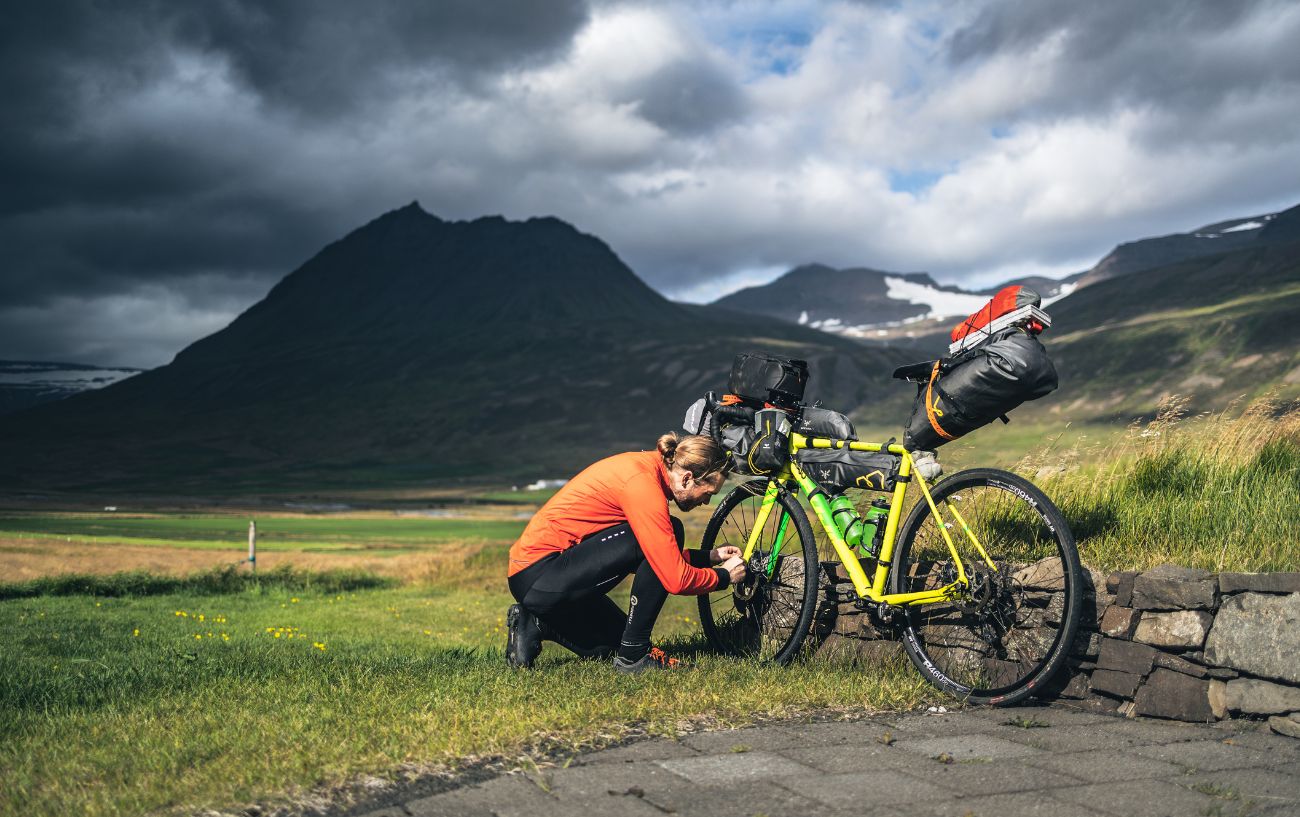 A man wearing orange is kneeling next to his touring bicycle.