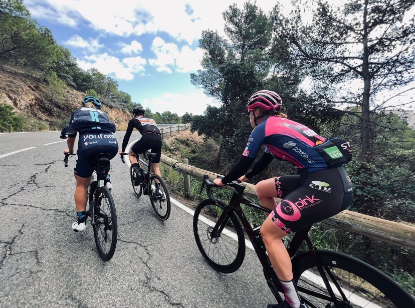 I ride a black road bike up a steep incline behind two fellow professional cyclists on a training ride in Girona.