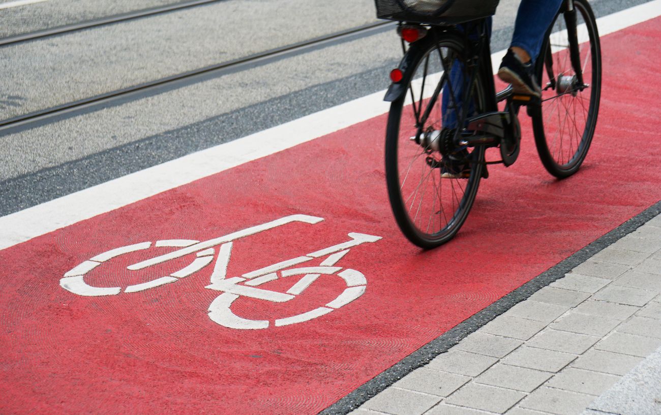 A cyclist rides a black bike on a red-tarmac cycling lane.