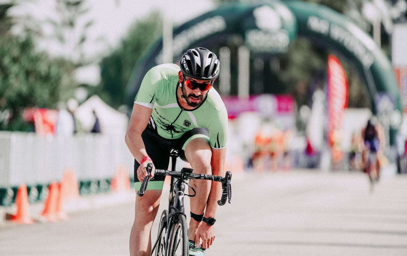 A cyclist reaches for his ankle in pain due to muscle imbalances.