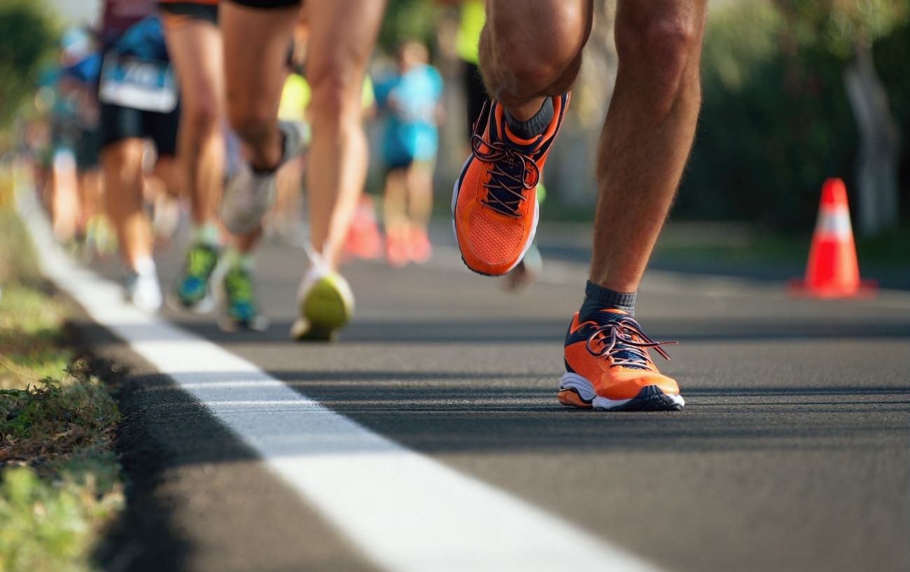 A close up of a runners orange shoes with other runners in the background.