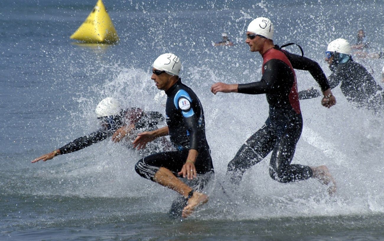 Simmers wearing wetsuits, goggles and caps run into the water.