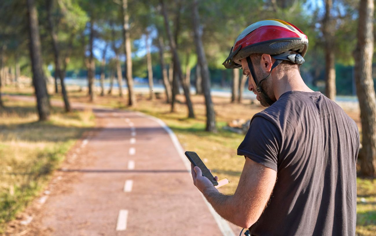 A cyclist wearing a helmet looks at his phone while on the bicycle.