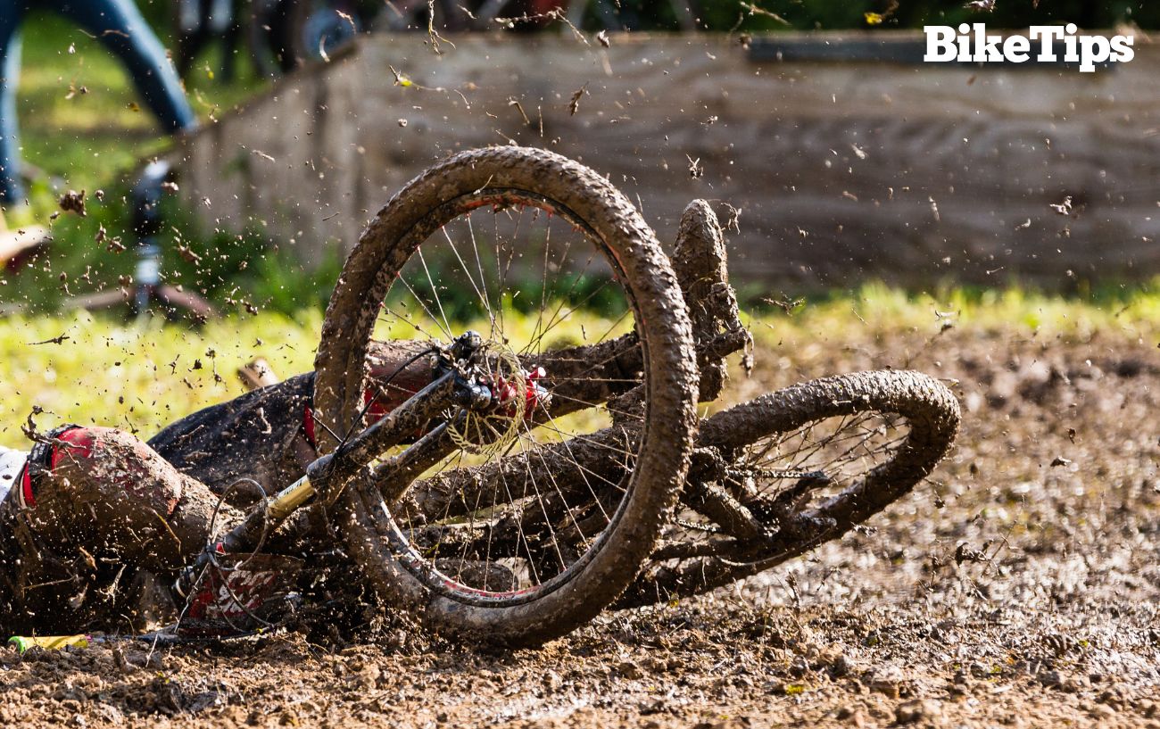 A cyclist falls over while riding in the mud.