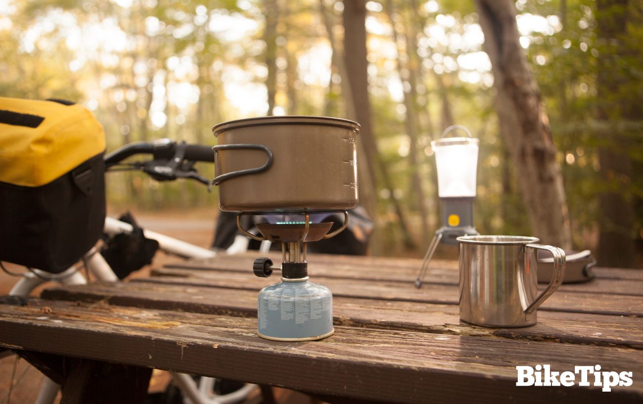 Cooking gear for bike camping on a wooden bench next to a bike.