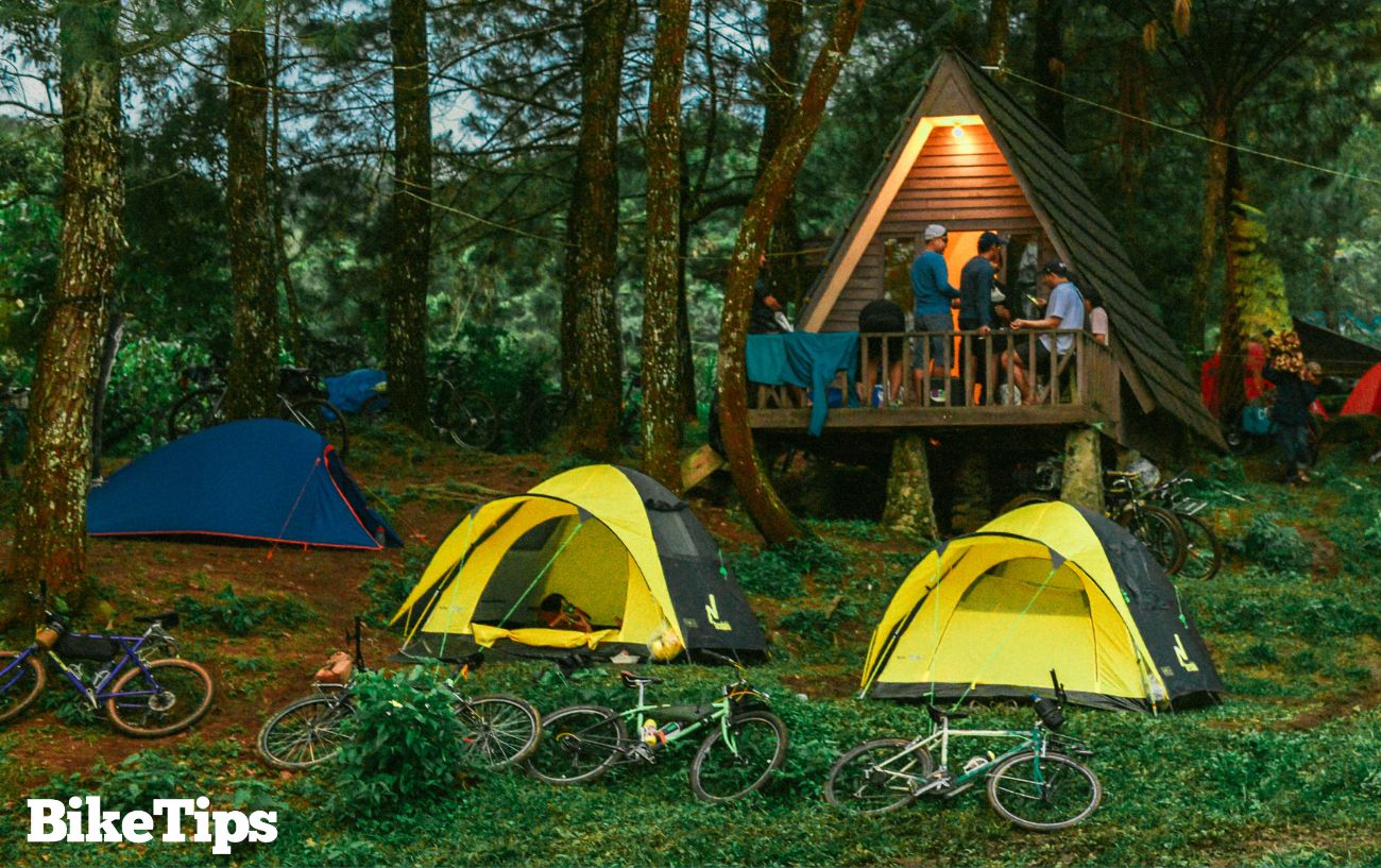 Bike camping in a forest with a group socialising in a hut.