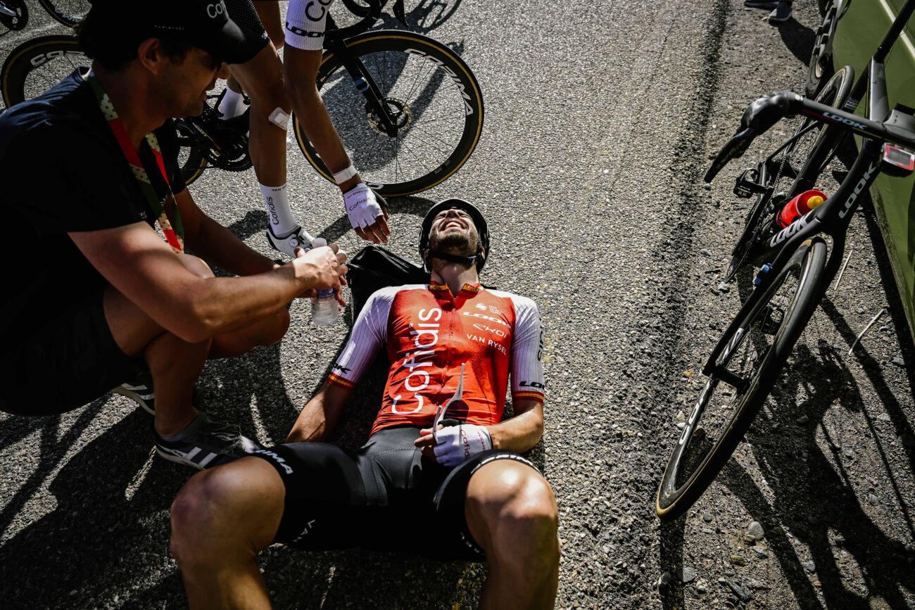A soigneur attends to a cyclist lying on the ground after a race.