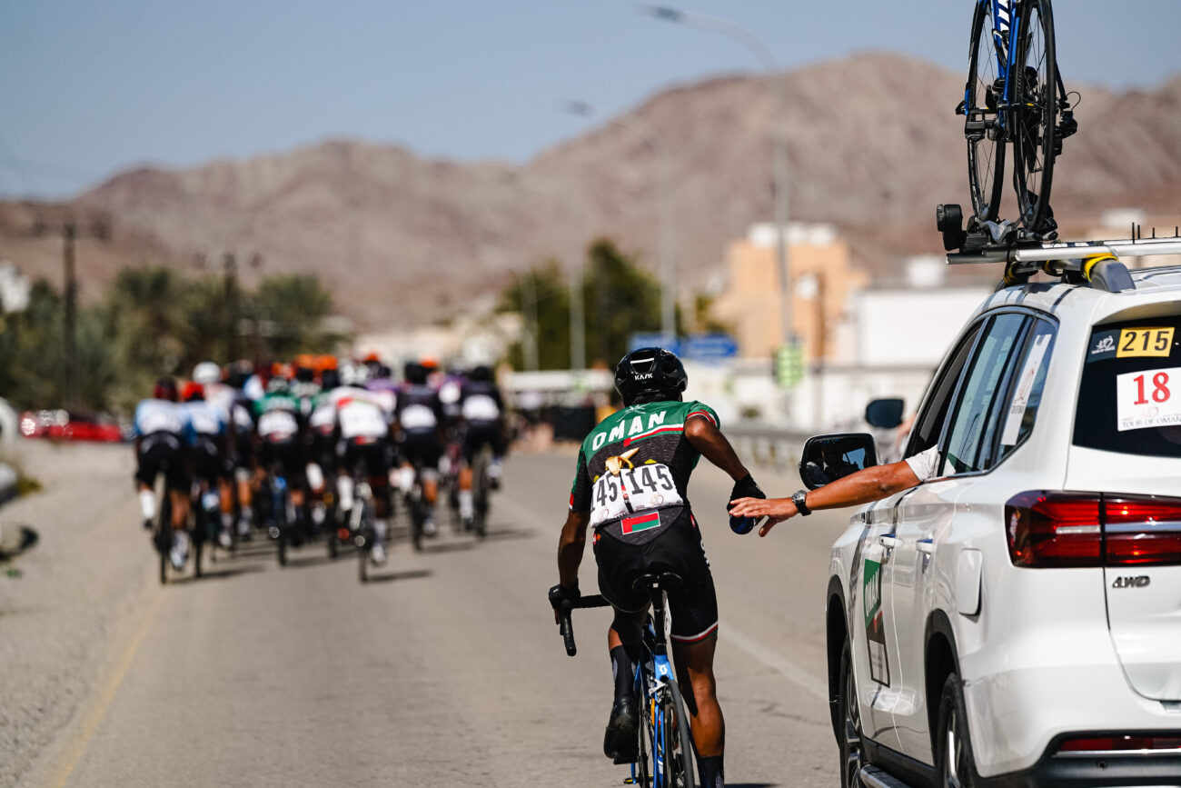 A cyclist is passed a water bottle from a team car during a race.
