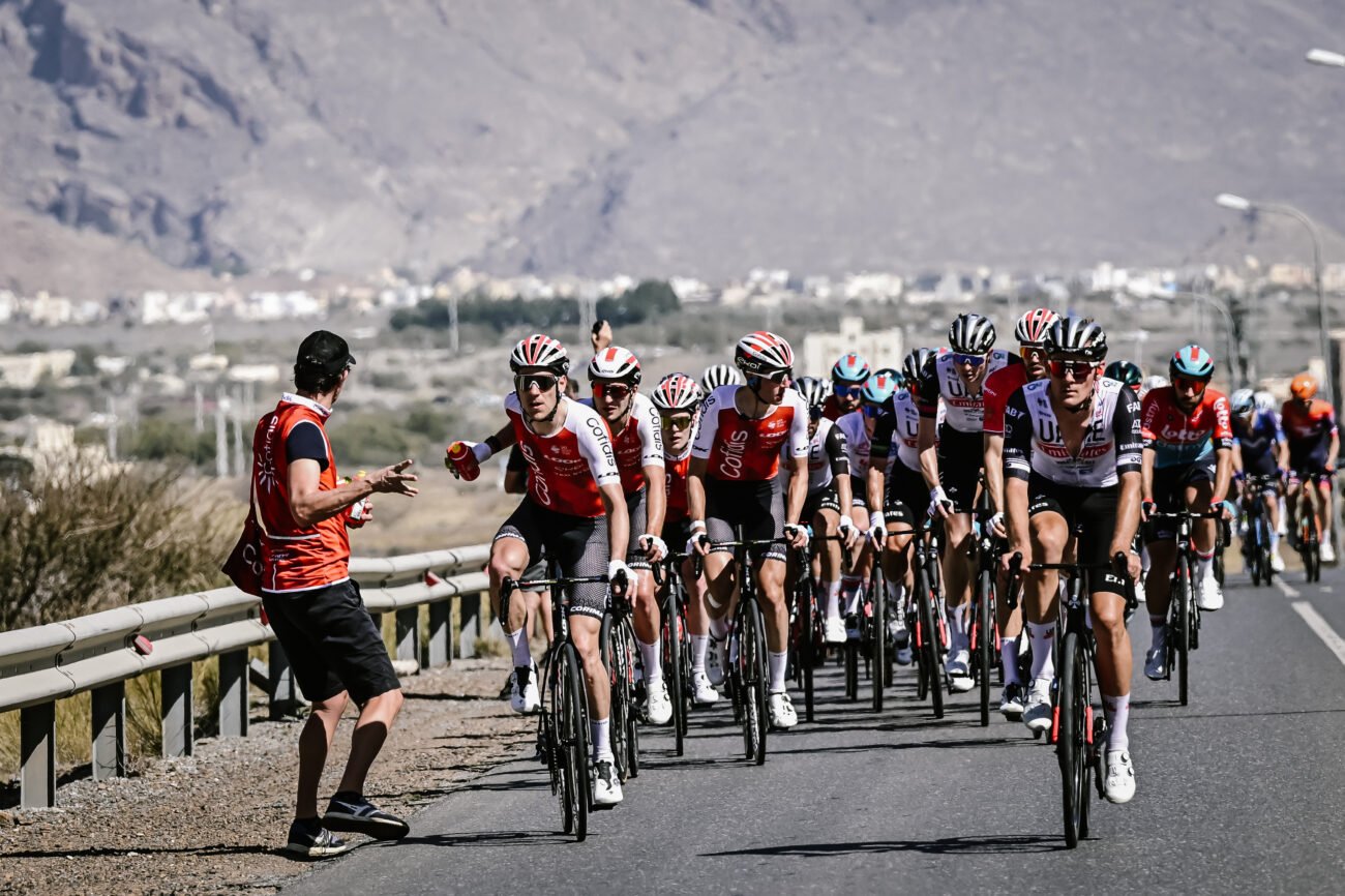 A soigneur hands a water bottle to one of their team's riders.