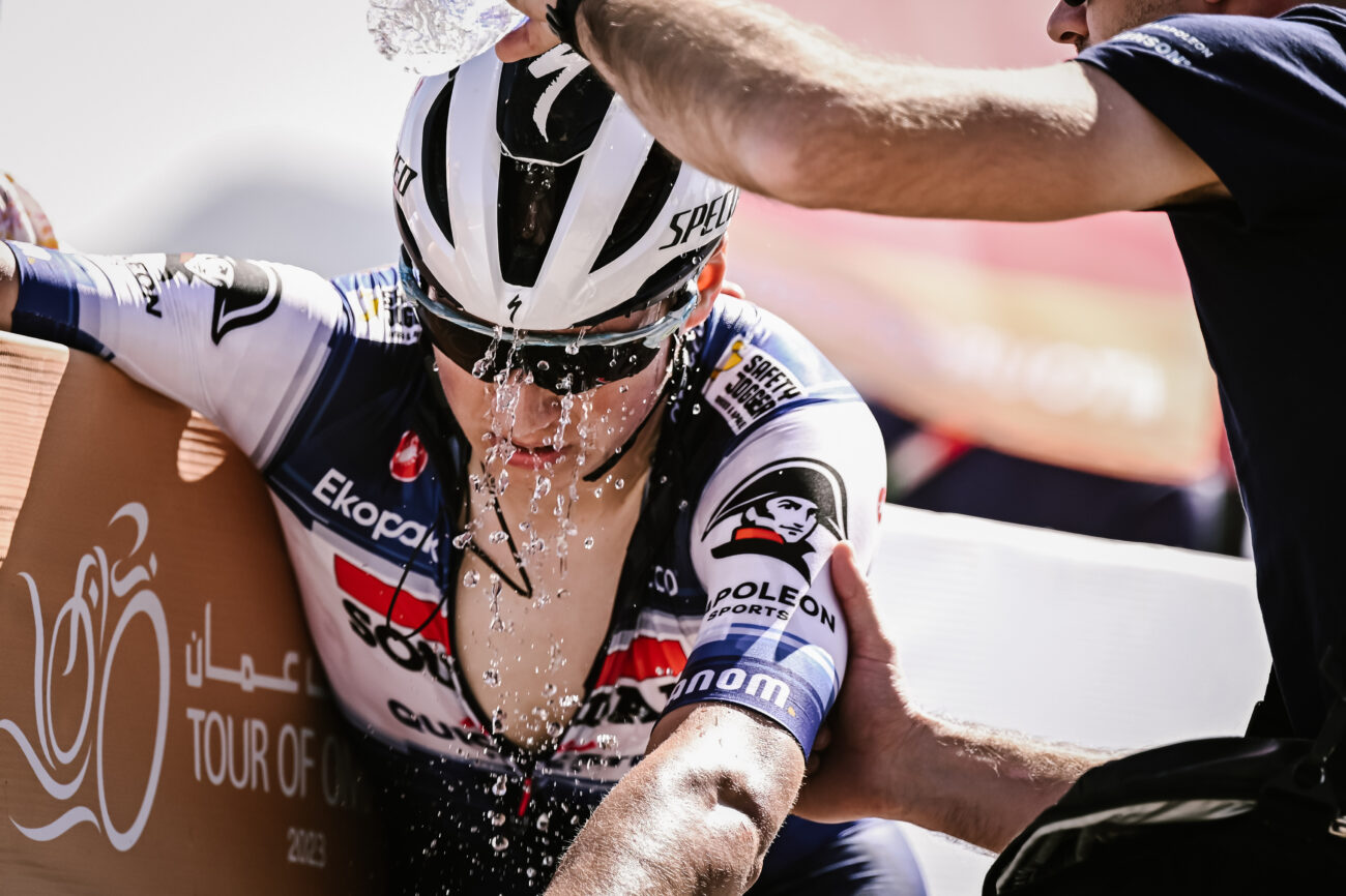 A soigneur pours a bottle of water over a cyclist to cool off.