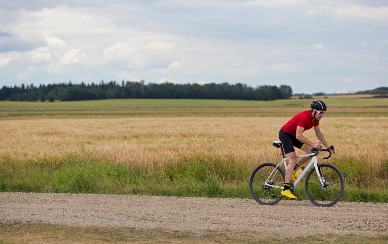 A man wearing red cycles along a gravel path.