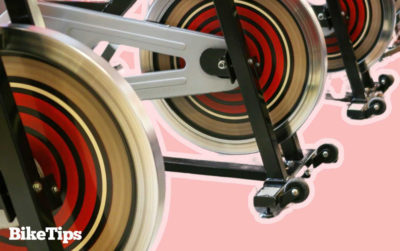 Three spin bikes in a row, with a pink background.
