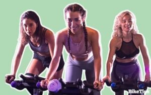 What is a spin class? Three women on exercise bikes work out at a gym against a green background.