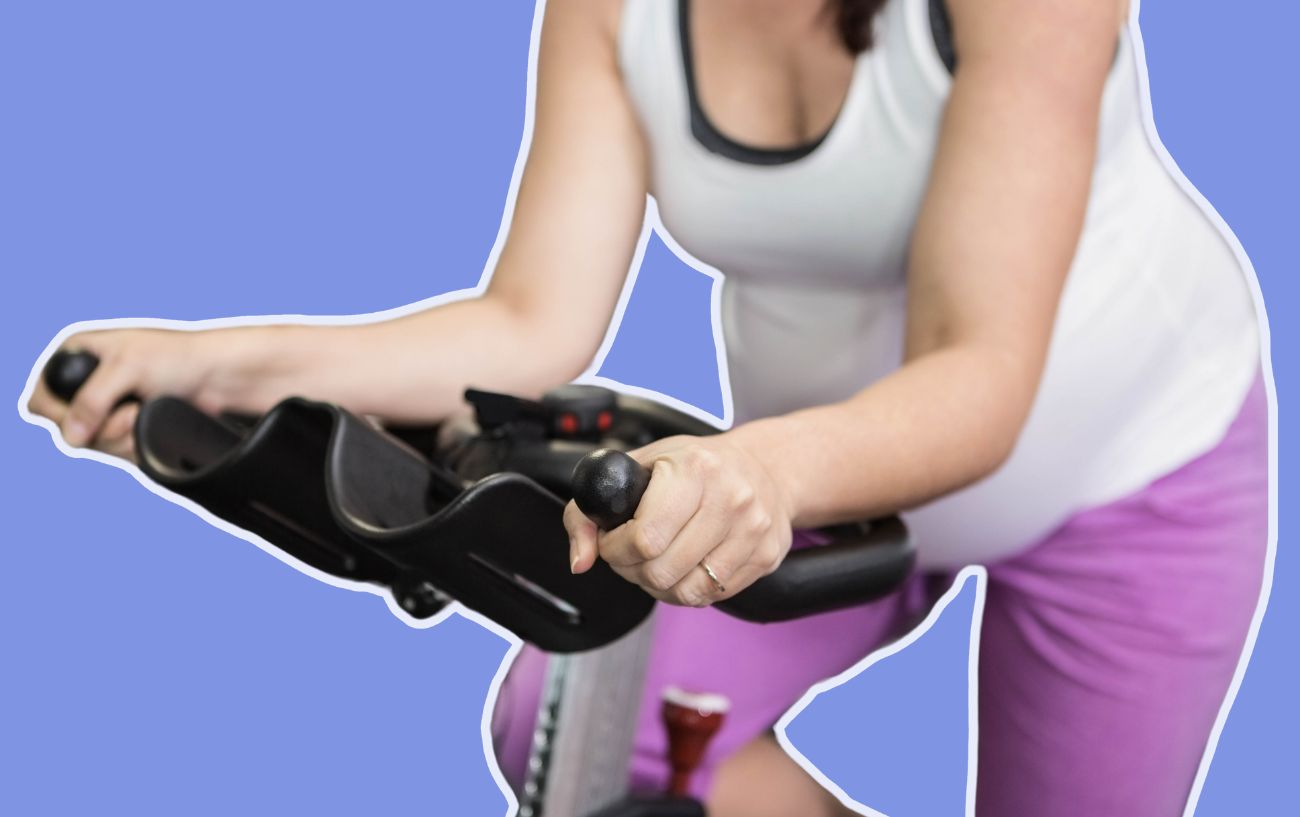 Ben Gibbons 2 A pregnant woman rides an exercise bike on a purple background.