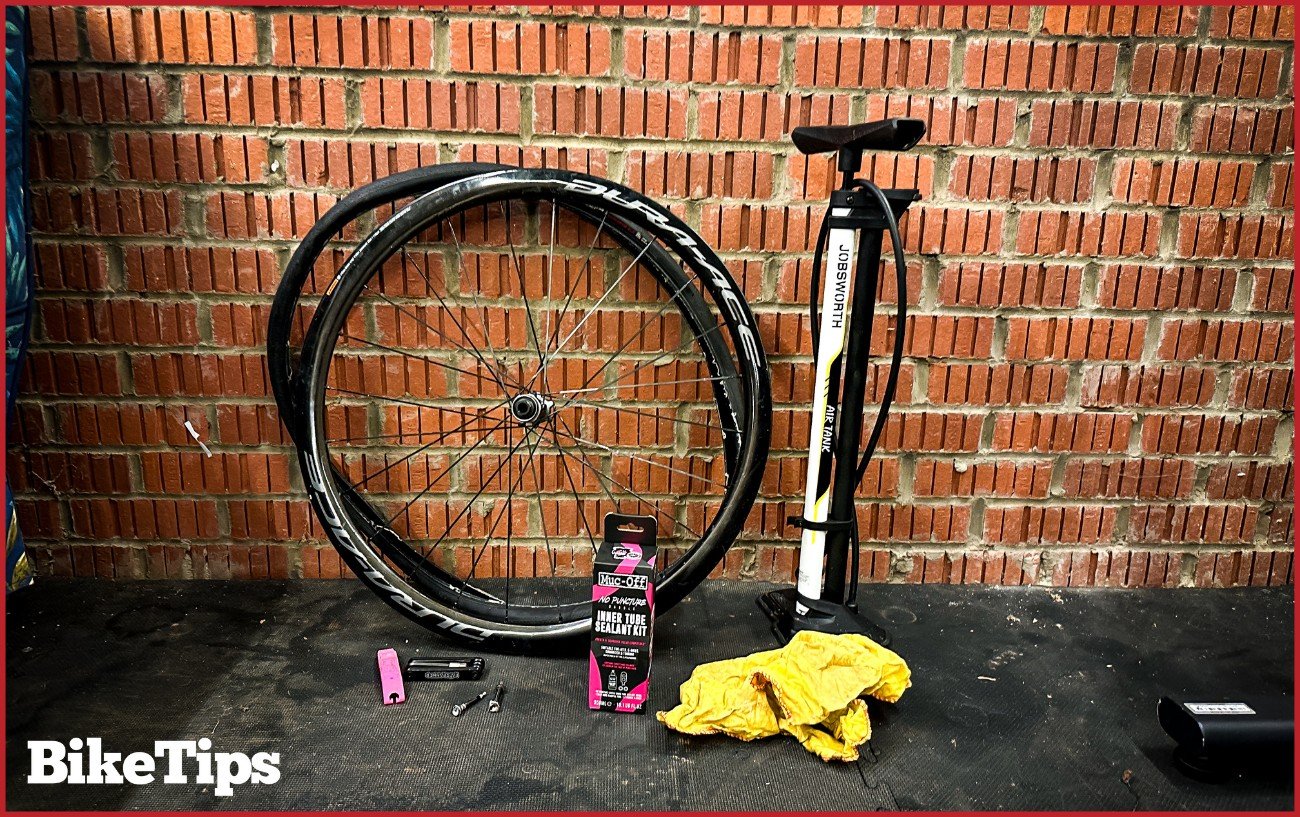 Photo showing all the equipment you'll need when learning how to install tubeless tires: a tubeless rim, tire, pump, sealant kit, valves, tire lever, sealant kit, and a cloth.
