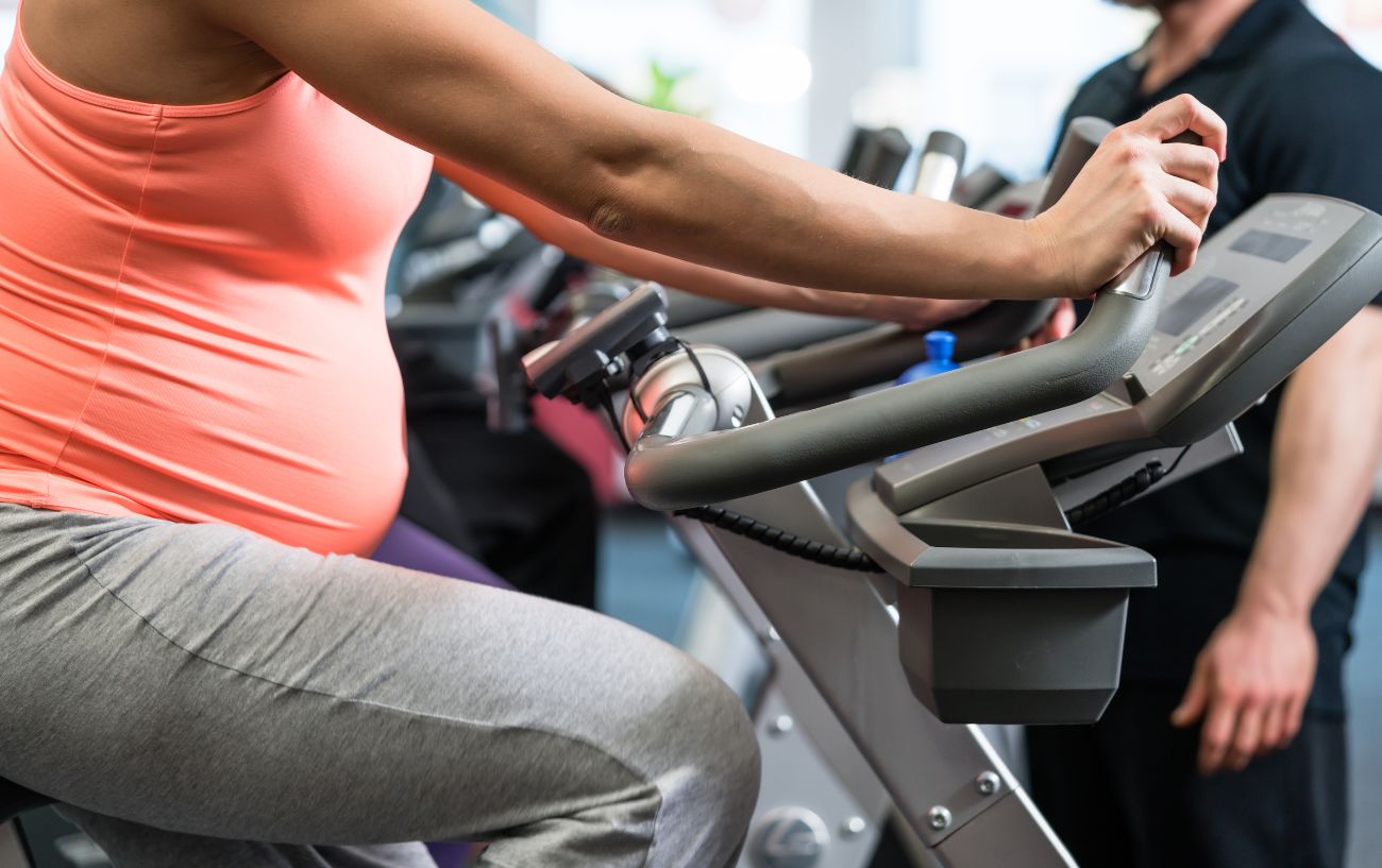Pregnant woman in an orange top rides an exercise bike.