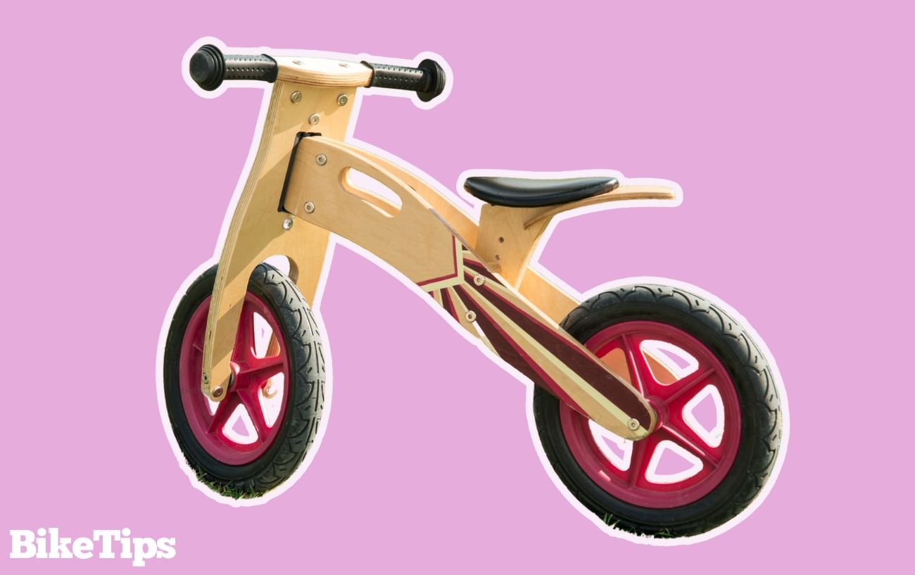 Photo of a wooden balance bike on a pink background.