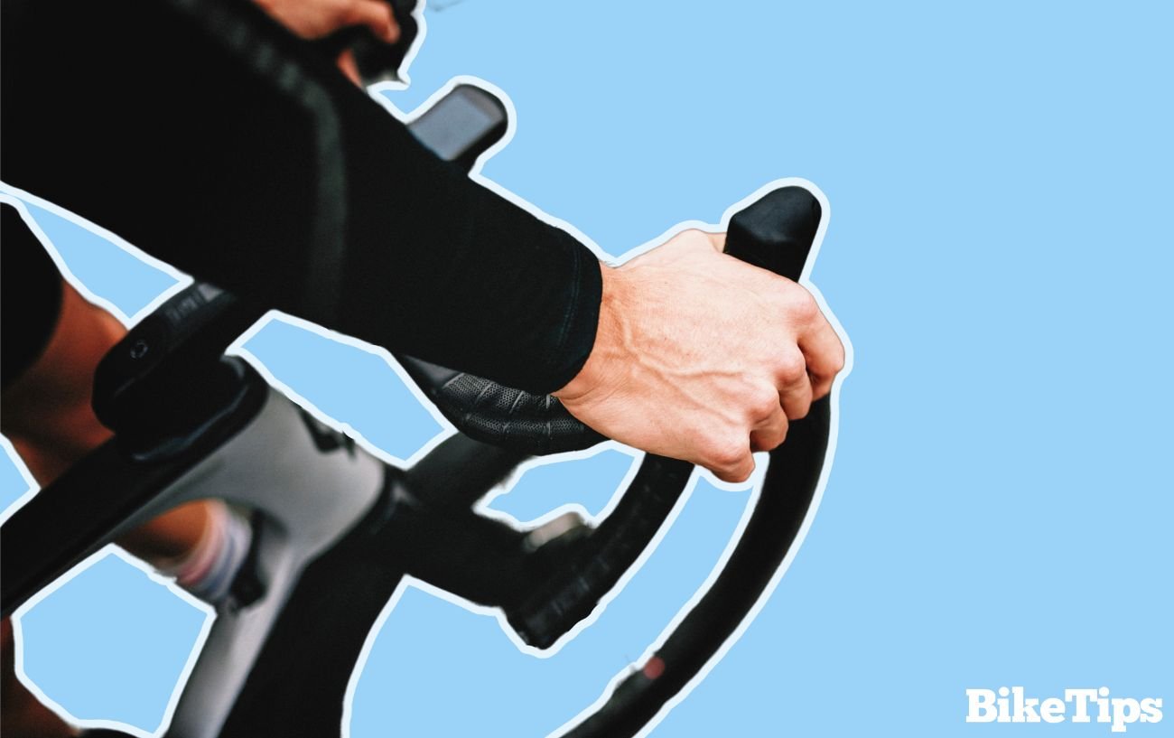 Ben Gibbons 3 Close-up of a cyclists hands on a bike's handlebars on a blue background.