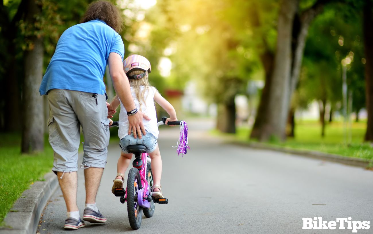 Photo with a parent demonstrating how to teach a child to ride a bike.